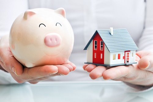 person holding piggy bank in one hand and mini house in the other