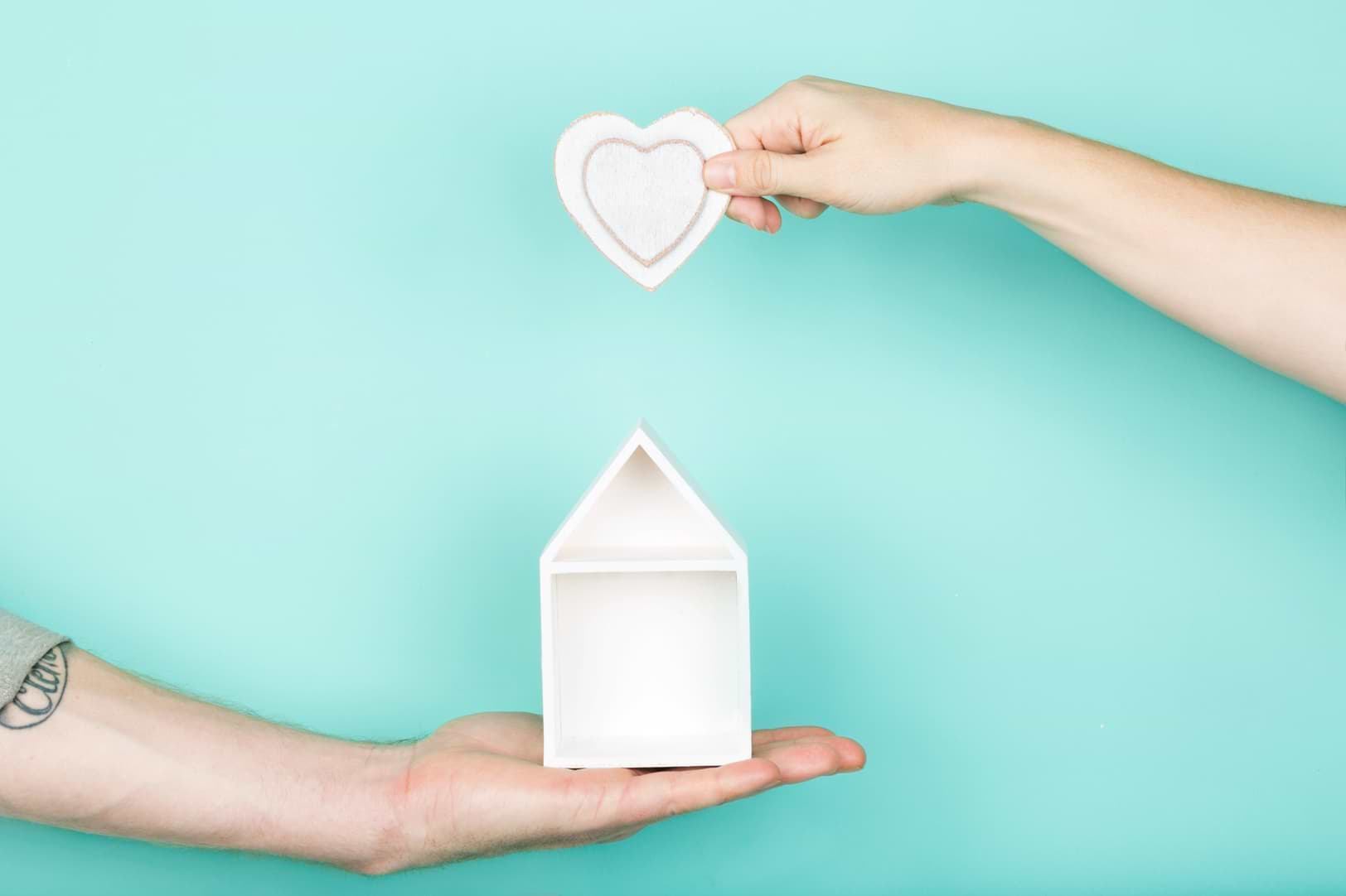 one handing holding a small house and another hand holding a heart cutout